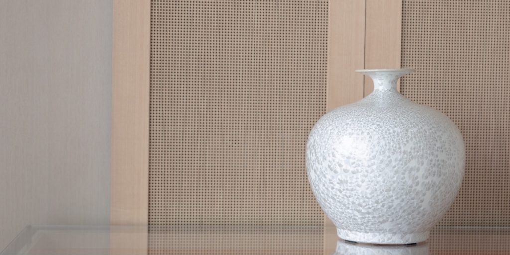Commode simple et épurée en bois et en verre surplombé d'un vase aux textures uniques.